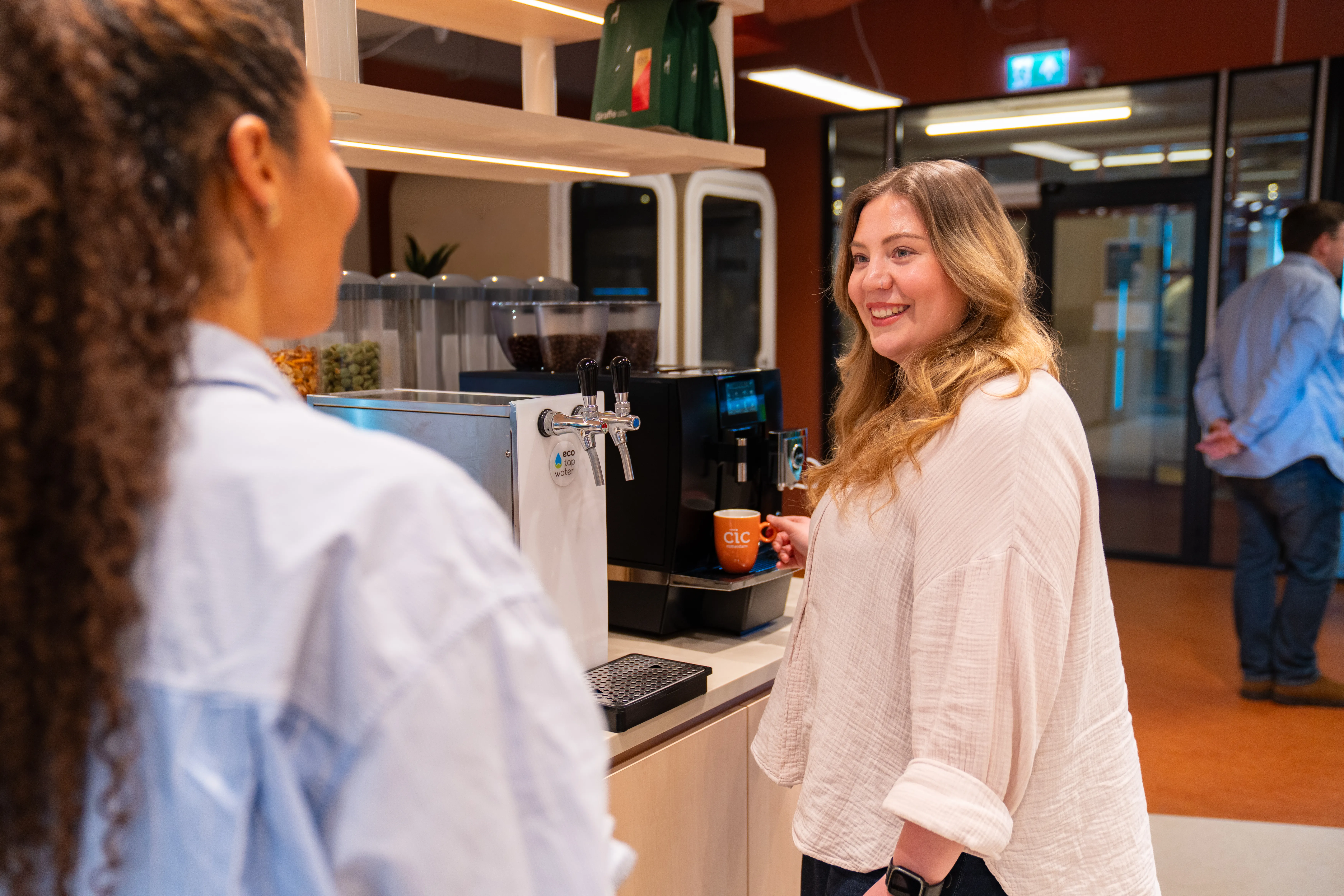 Twee collega's in gesprek bij de koffiemachine op kantoor